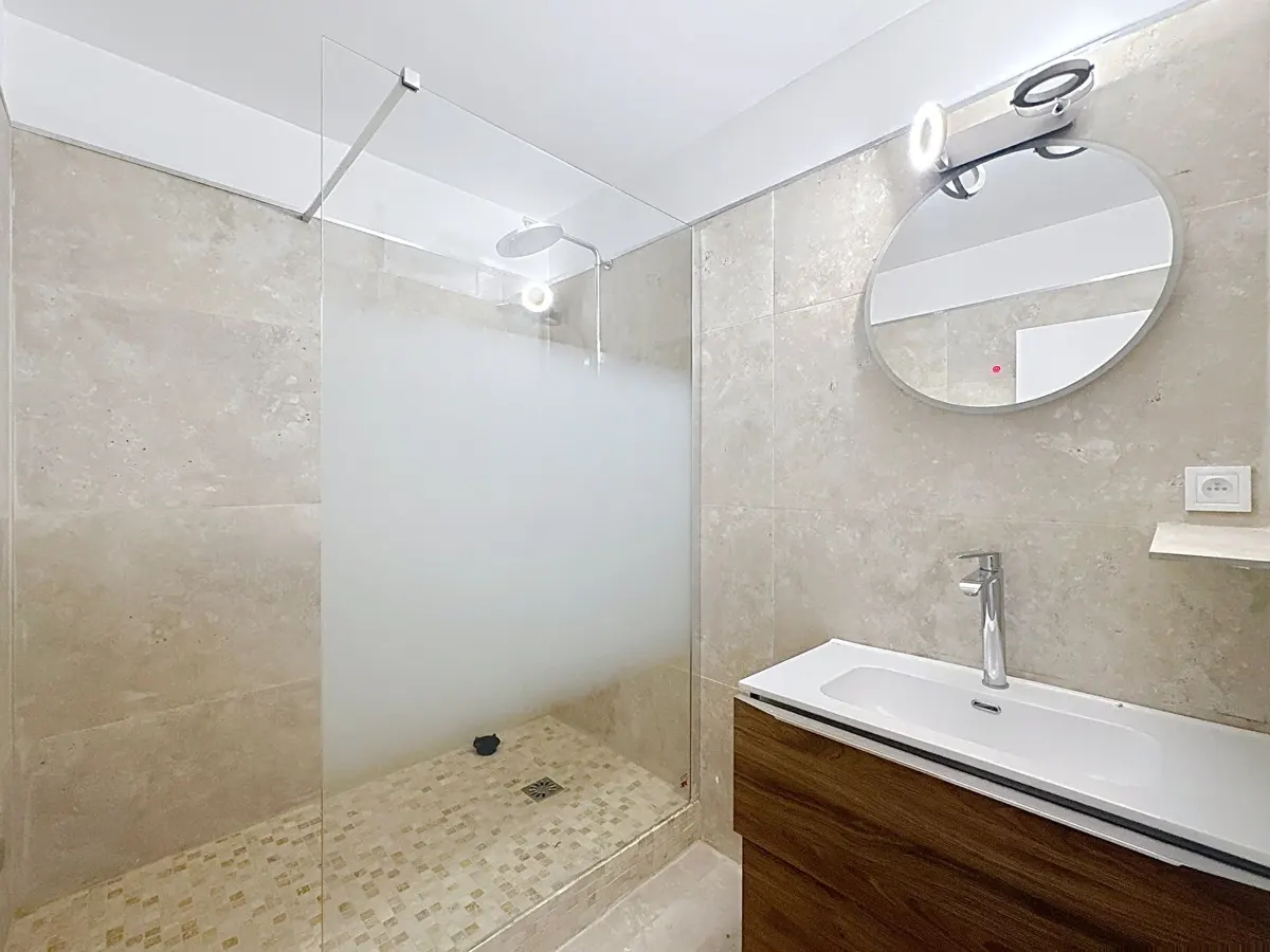 Salle de bain avec paroi de douche, vasque en bois et miroir rond